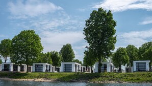 A row of modern, white cabins by a river, with large windows and doors, surrounded by trees. - Holiday Home in Netherlands With Water Views (Maurik)