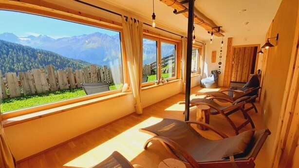 A sunlit room with wooden furniture, large windows, and a view of mountains. - the Veitenhof Comfortable Holiday Residence (Umhausen)