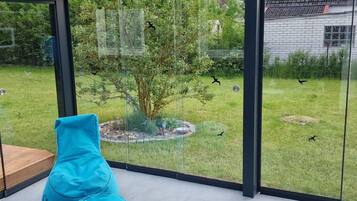 A modern room with a glass wall, a blue bean bag chair, and a view of a garden with a tree and birds.