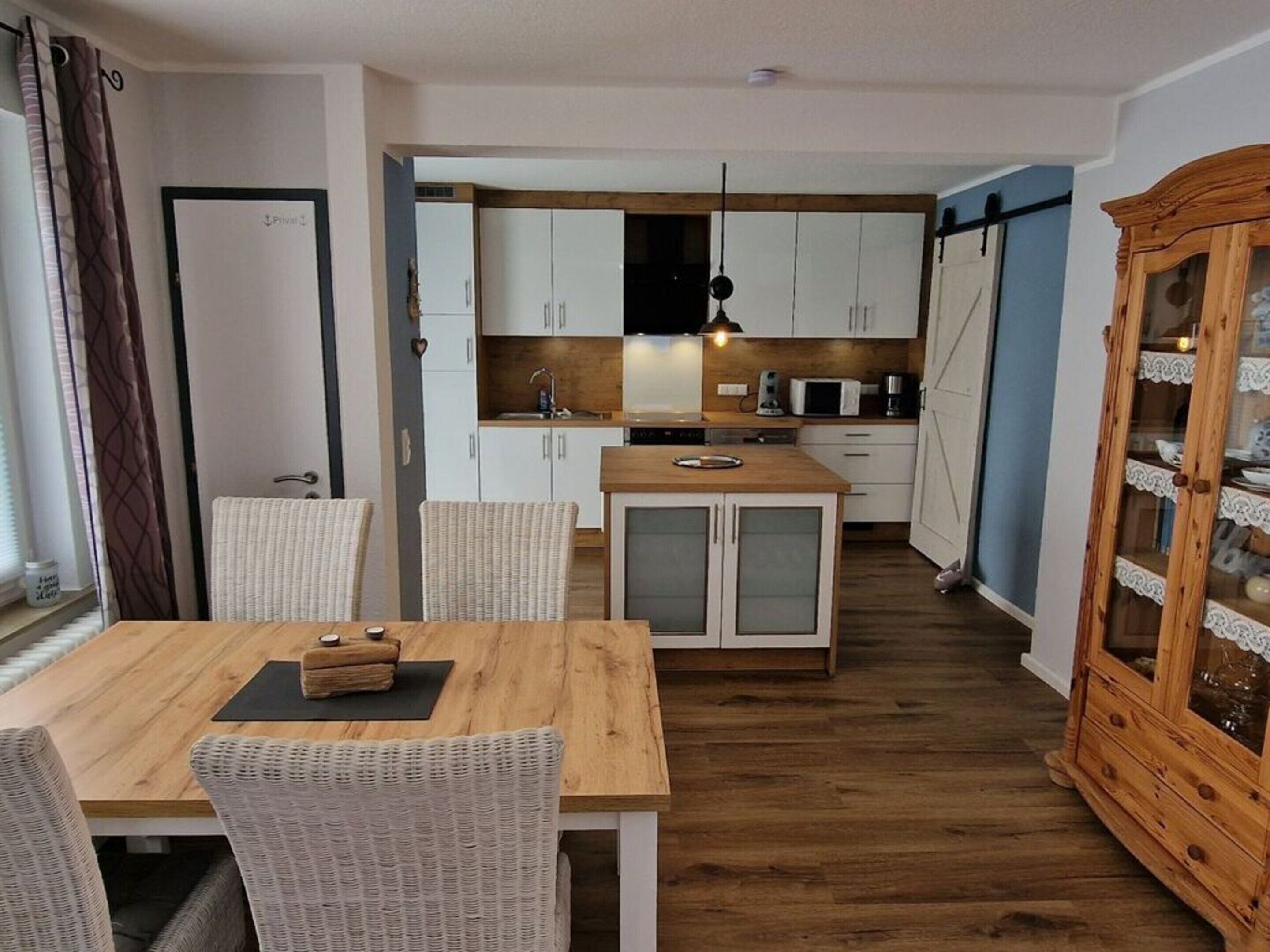 A compact kitchen with white cabinets, a wooden island, and a dining area with wicker chairs.