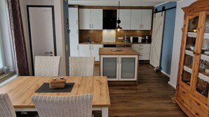A compact kitchen with white cabinets, a wooden island, and a dining area with wicker chairs. - Beach Chair No.1 Comfortable Vacation Home (Wangerland)