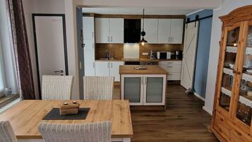 A compact kitchen with white cabinets, a wooden island, and a dining area with wicker chairs.