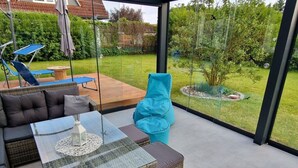 A modern outdoor living space with a glass table, wicker furniture, and a view of a garden. - Beach Chair No.1 Comfortable Vacation Home (Wangerland)