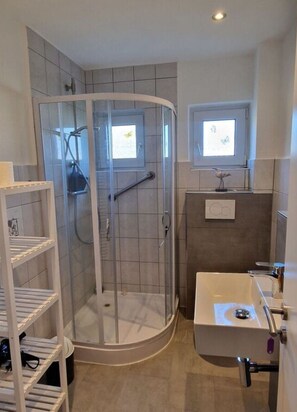 A modern bathroom with a glass-enclosed shower, a sink with a mirror, and a small window above the mirror. - Beach Chair No.1 Comfortable Vacation Home (Wangerland)