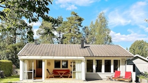 Ein eingeschossiges Haus mit Ziegeldach, einer überdachten Veranda mit roten Stühlen und einem Rasen im Vordergrund.