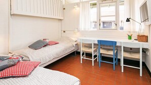 Een kamer in studentenresidentie met twee eenpersoonsbedden, een bureau met stoel, een raam met gordijnen en een tv aan de muur.