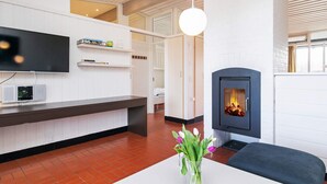 Een moderne woonkamer met een open haard, een flatscreen televisie aan de muur en een witte tafel met een bloemenvaas.