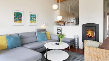 A modern living room with a grey sectional sofa, a round coffee table, a wicker armchair, and a fireplace.