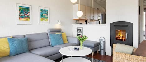 Una sala de estar moderna con un sofá seccional gris, una mesa redonda de centro, un sillón de mimbre y una chimenea.