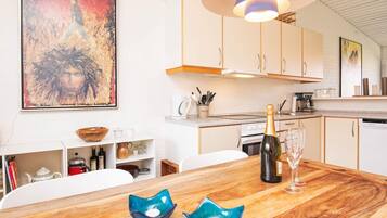 A modern kitchen with white cabinets, a wooden dining table, and a large painting on the wall.