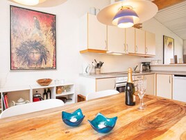 A modern kitchen with white cabinets, a wooden dining table, and a large painting on the wall.