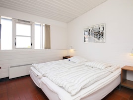 Un dormitorio con cama, ventana, radiador, luz empotrada en la pared y un cartel.