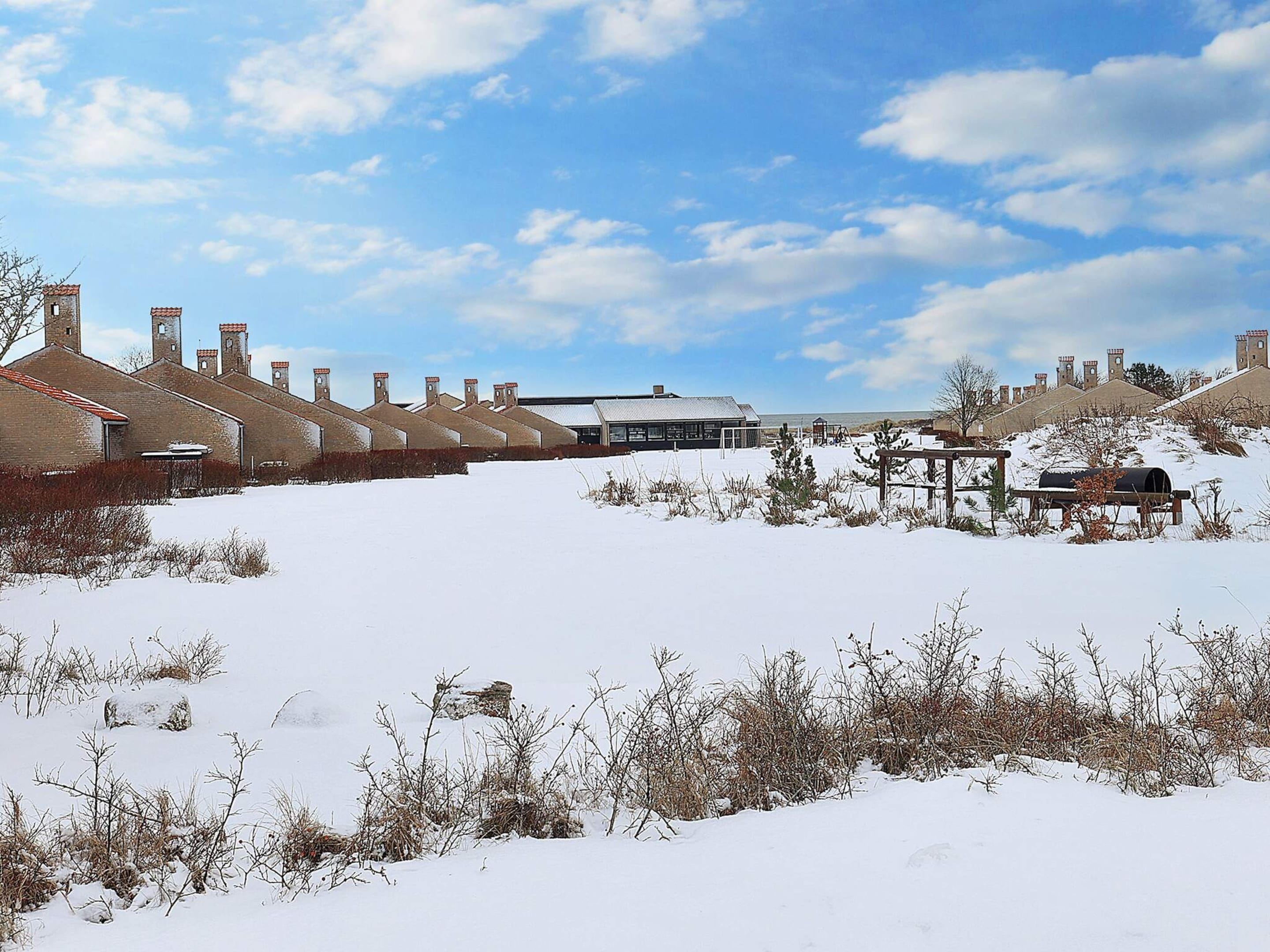A snow-covered landscape with a row of brick buildings and a modern structure in the background.
