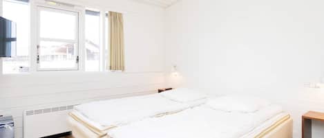 A room with two beds, a window, a heater, and a small table.