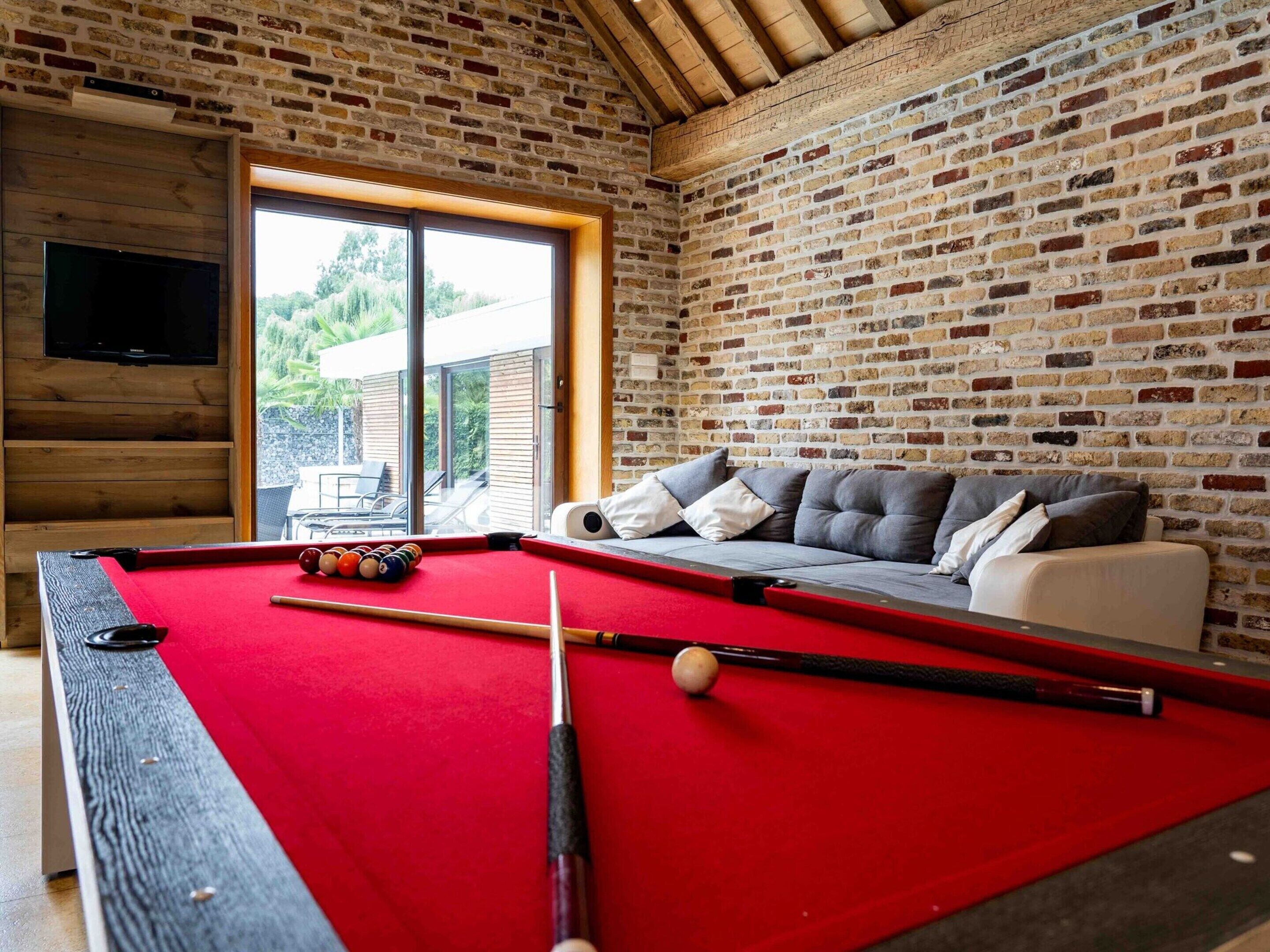A pool table with balls, a sofa with cushions, a television, and a brick wall.