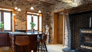 A rustic kitchen with exposed brick walls, a central island with stools, a fireplace, and a statue. - Villa With Swimming Pool in Erembodegem (Aalst)