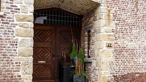 A brick building with a large wooden double door, a small window, and a potted plant. - Villa With Swimming Pool in Erembodegem (Aalst)