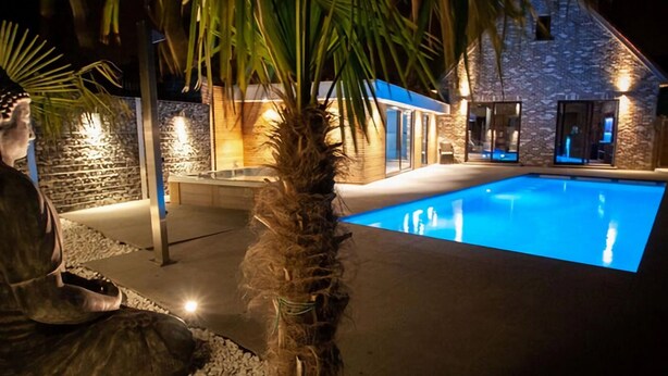 A nighttime view of a swimming pool area with a stone building, palm trees, and a statue. - Villa With Swimming Pool in Erembodegem (Aalst)