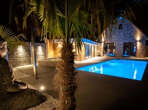 A nighttime view of a swimming pool area with a stone building, palm trees, and a statue. - Villa With Swimming Pool in Erembodegem (Aalst)