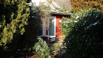 A red building with a white door, surrounded by dense greenery and snow-covered plants.