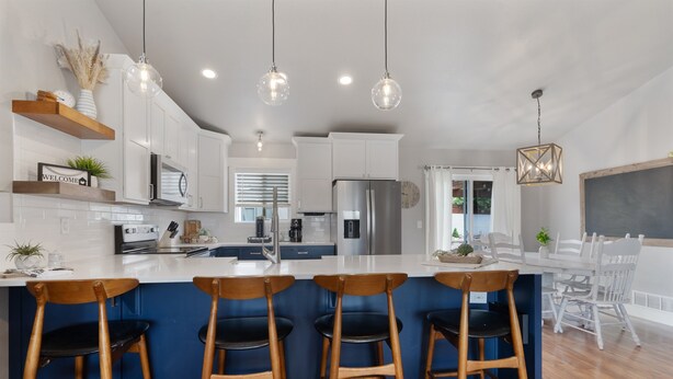 Una cocina moderna con una isla central, taburetes de bar, iluminación colgante y un comedor con pared de pizarra.