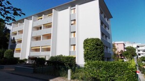 Un immeuble moderne à plusieurs étages, doté de balcons, entouré de verdure et surplombant un ciel dégagé.