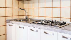 Une cuisine équipée d’une cuisinière à gaz, d’un évier en acier inoxydable et de meubles blancs.
