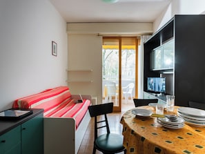 A compact living space with a sofa, a dining table, a TV, and a kitchenette.
