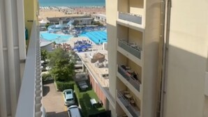 A high-rise building with balconies overlooking a beach, pool, and parking area. - Seaside bliss modern comfort with sea view (Bibione)