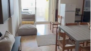 A compact living space with a sofa, a dining table with chairs, a ceiling fan, a TV mounted on the wall, and a sliding glass door leading to an outdoor area. - Seaside bliss modern comfort with sea view (Bibione)