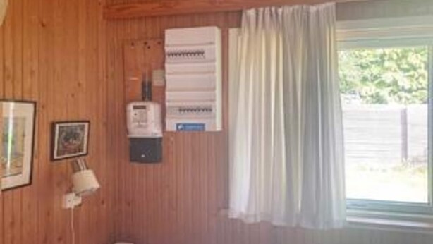 A room with wooden walls, a window with curtains, a heater, and a framed picture. - 6 Person Holiday Home in Rorvig (Rørvig)