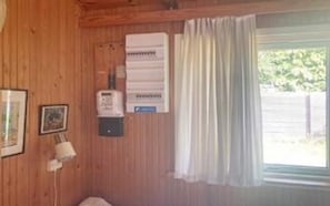 A room with wooden walls, a window with curtains, a heater, and a framed picture.