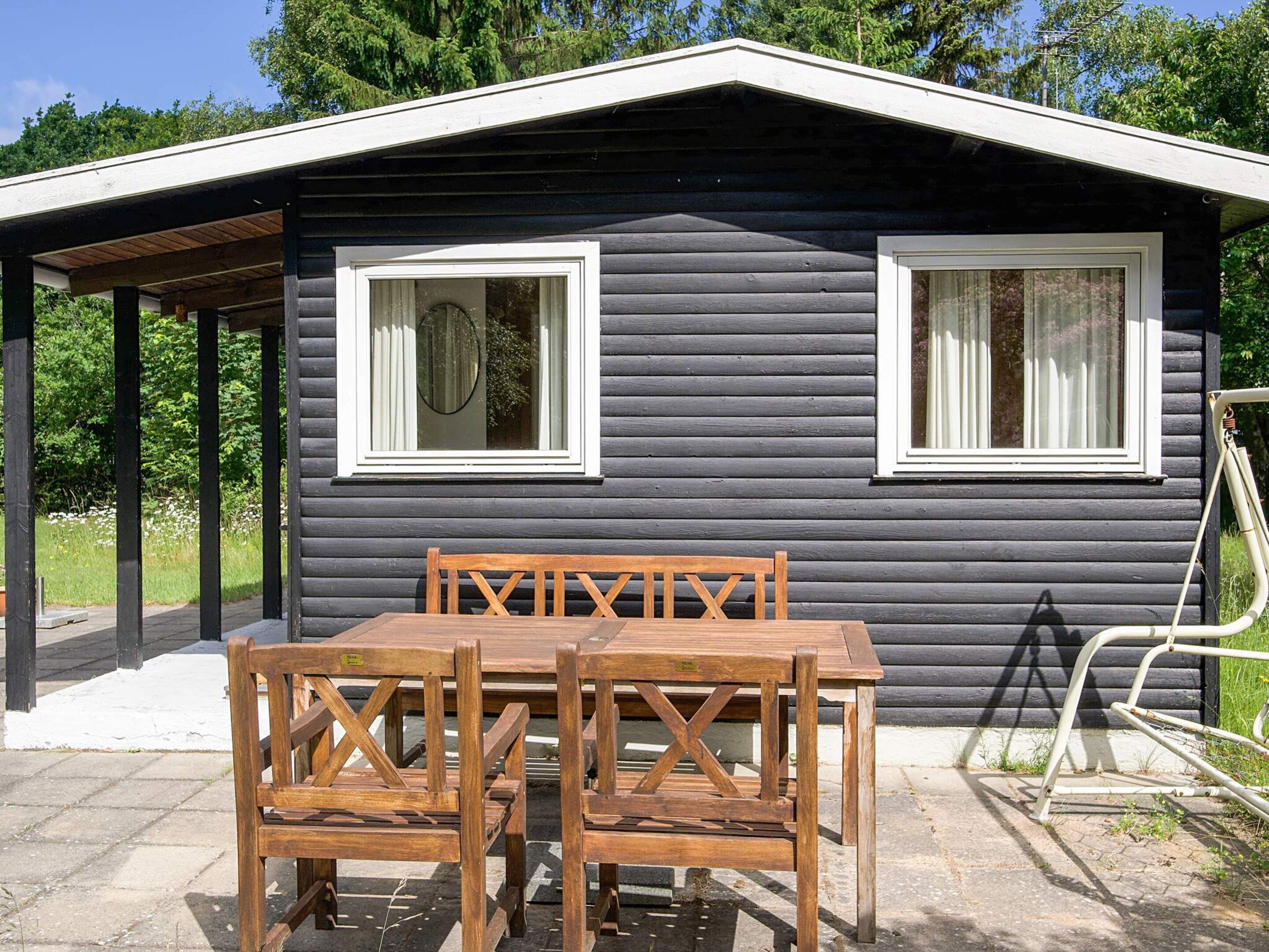 A cabin with two windows, a covered patio, and a table with chairs.