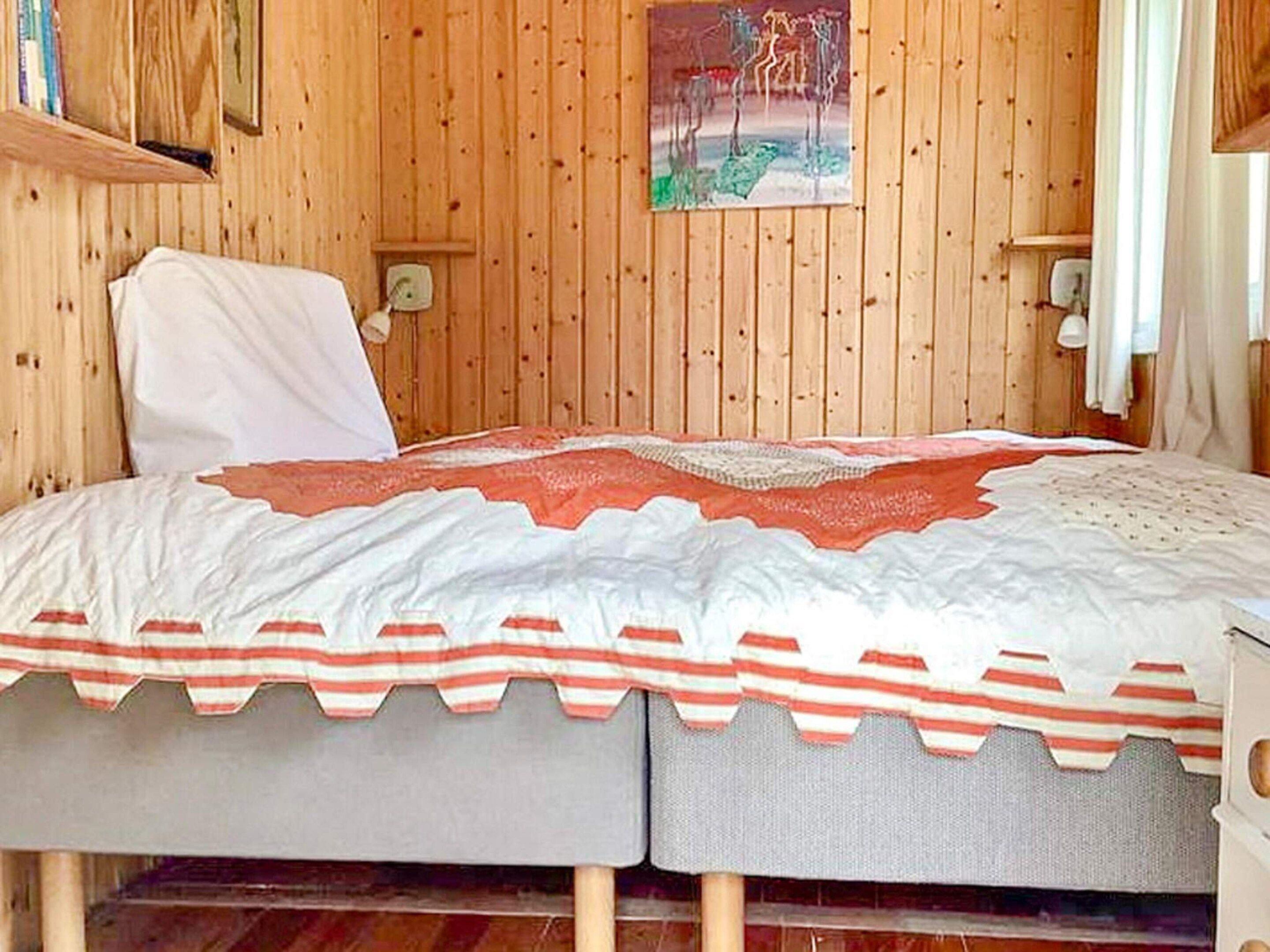 A wooden-paneled room with a bed featuring a striped bedspread and a decorative pillow.