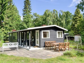 A small cabin with a covered porch, a dining table with chairs, and a bench.
