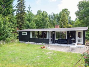 A small, single-story house with a covered porch, large windows, and a garden area.