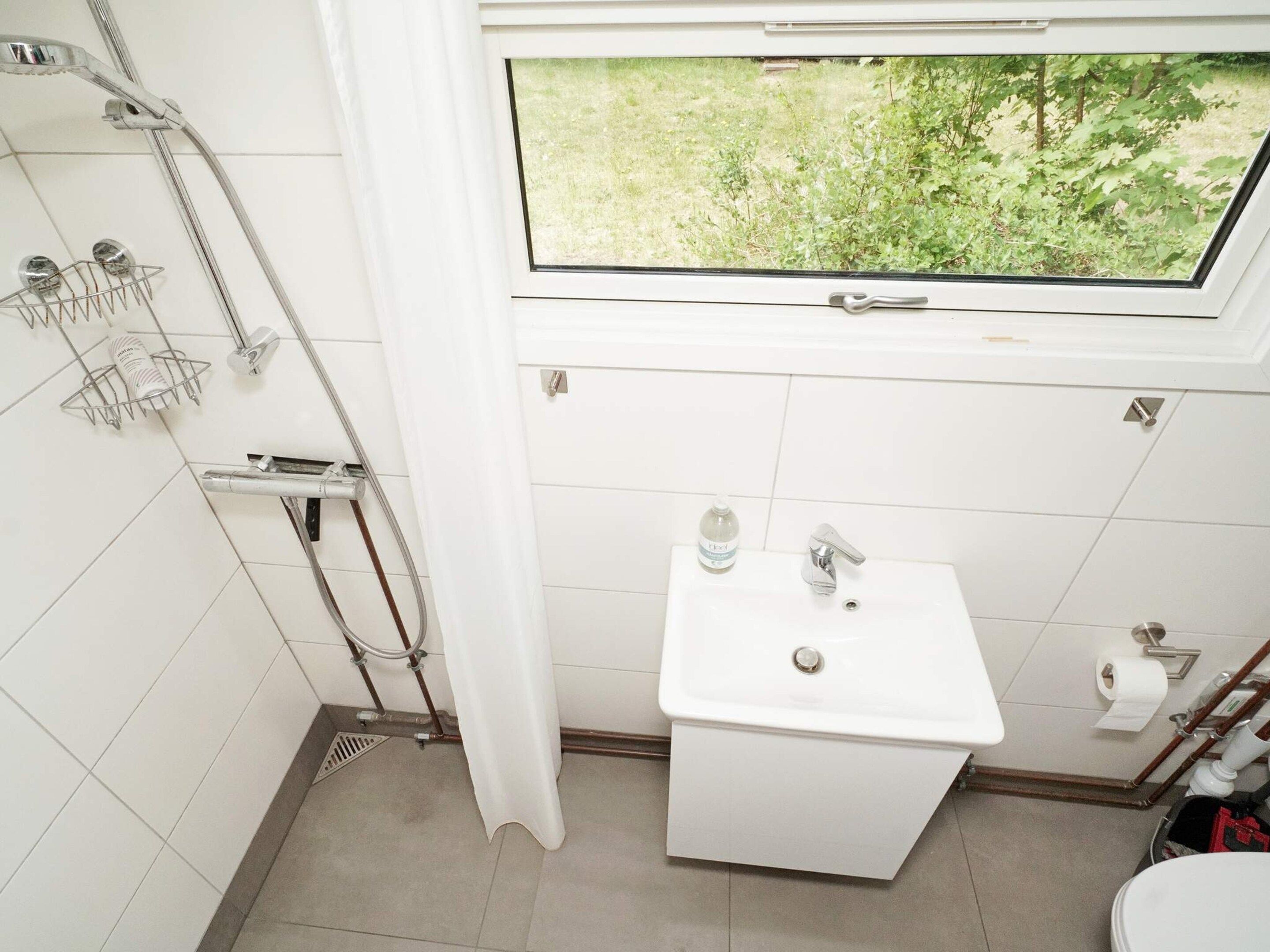 Ein Badezimmer mit Fenster, Waschbecken, Dusche und Toilette.