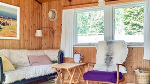 A cozy cabin interior with a wooden wall, a sofa, a chair, a small table, and a window with a view of greenery. - 6 Person Holiday Home in Rorvig (Rørvig)