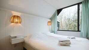 Ein Schlafzimmer mit einem großen Bett, zwei Wandlampen, einem Fenster mit Vorhängen und einem weißen Nachttisch.