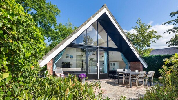 Ein modernes Haus mit einem Satteldach, großen Glasfenstern und einer Terrasse mit Gartenmöbeln.