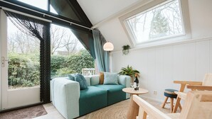 Ein modernes Wohnzimmer mit einem türkisfarbenen Sofa, Holzmöbeln, einem runden Couchtisch und Blick ins Grüne.