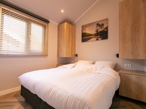 A bedroom with a bed, wooden headboard, bedside tables, and a wall-mounted painting. - Luxury Lodge With Private Swimming Pool (Rhenen)