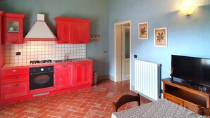Een kleine keuken met rode kastjes, een gasfornuis en een betegelde spatwand.