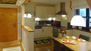 A modern kitchen with wooden cabinets, a stove, and a dining area with a table set for two. - Hofatsblick With Sauna (Fischen im Allgaeu)
