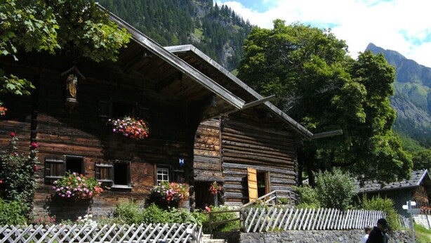 A rustic wooden cabin with a stone foundation, wooden steps leading to the entrance, and a white picket fence. - Hofatsblick With Sauna (Fischen im Allgaeu)