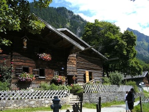 A rustic wooden cabin with a stone foundation, wooden steps leading to the entrance, and a white picket fence. - Hofatsblick With Sauna (Fischen im Allgaeu)