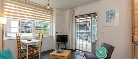 Ein modernes Wohnzimmer mit Essbereich, Fernseher und großem Fenster mit Jalousien.