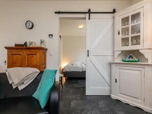 Een kamer met een zwarte leren bank, een houten kast, een witte schuifdeur en een klok aan de muur.
