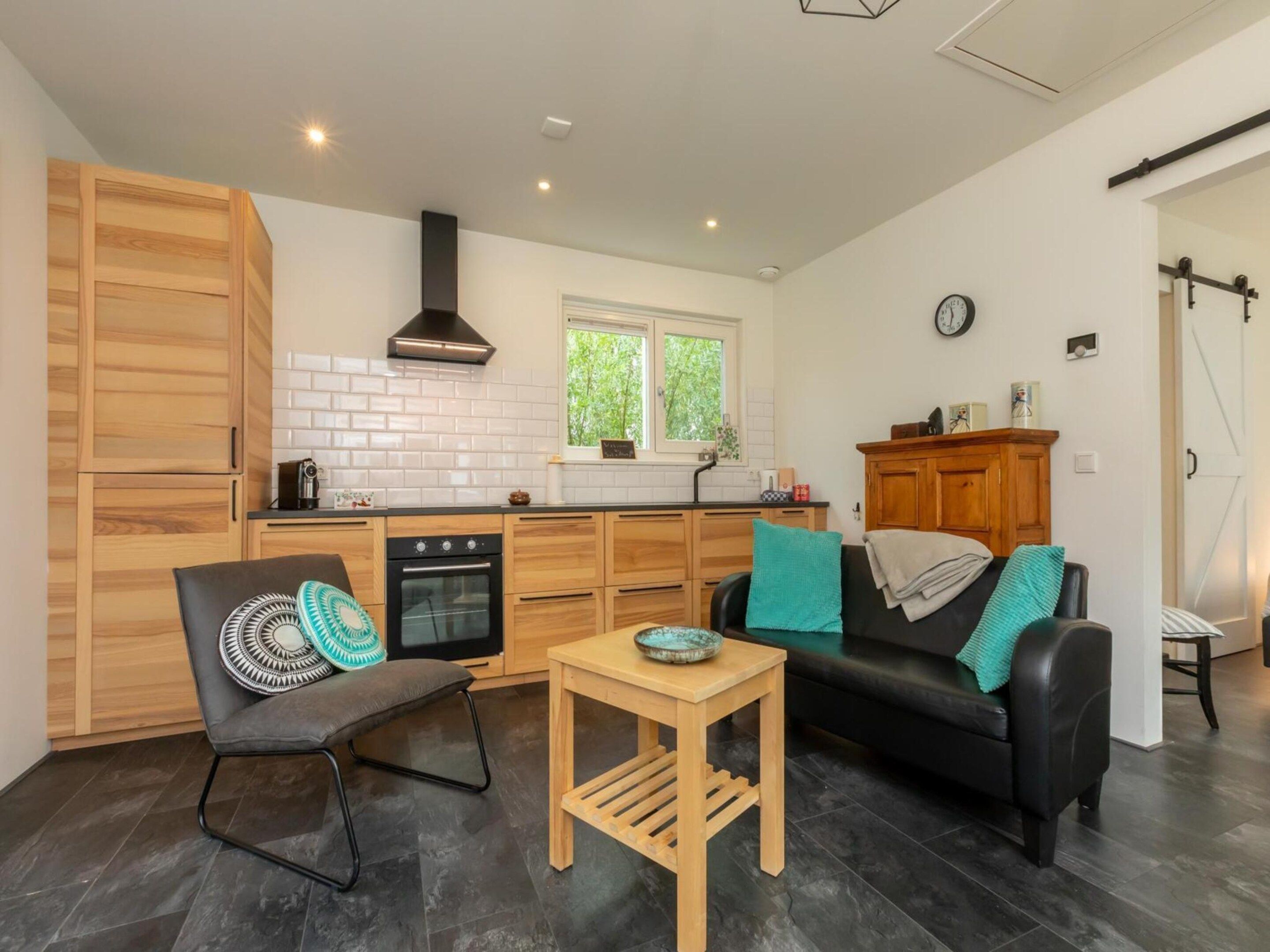 A compact kitchen with a built-in oven, a dining area with a small table and a sofa, and a window with a view of greenery.