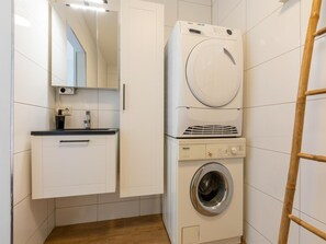 Une petite buanderie comprenant un lave-linge, un sèche-linge et un petit meuble de rangement.